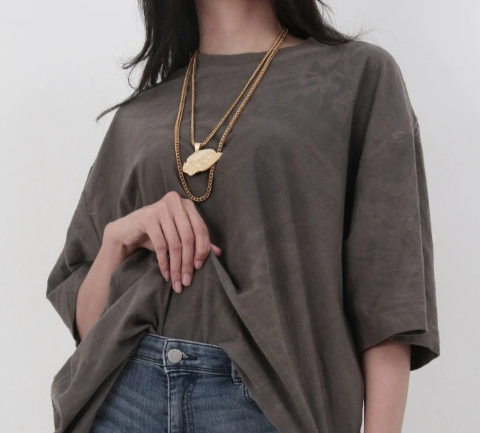 Woman in a loose t-shirt, jeans, and gold leaf necklace.